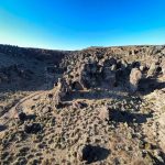 A rocky desert landscape near Gooding, ID, with rugged cliffs and sparse vegetation under a clear blue sky, illuminated by bright sunlight.