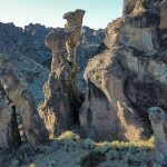 Large, rugged rock formations rise from a dry, grassy landscape under a clear sky in Gooding, ID, creating dramatic natural shapes and shadows in this striking desert or canyon setting.