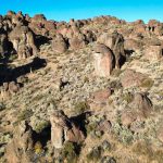 Rugged reddish-brown rock formations and sparse dry vegetation create a striking rocky desert landscape under a clear blue sky near Gooding, ID.